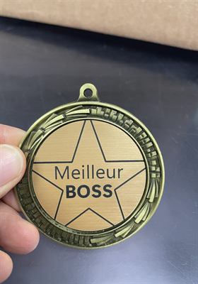 Médaille de laiton gravée d’une étoile et d’une mention humoristique, tenue à la main