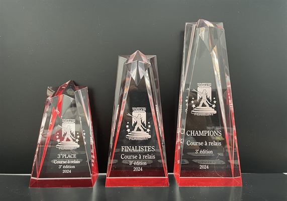 Trois trophées de cristal en obélisque à base rouge, gravés d’un logo de pompier et des mentions champions, finalistes et troisième place